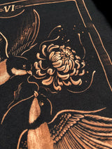 Close-up of a black bleach artfeaturing two birds and a large flower in a warm metallic copper or bronze tone. Tarot card design t-shirt VI: the lovers