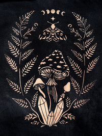 A stencil design painted with bleach on fabric featuring a stylized illustration of mushrooms, fern leaves, a crescent moon and a star motif at the top