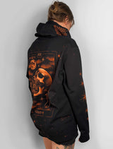A person shown from the back wearing a black hoodie with a large tarot card style graphic on the back in orange, brown, and cream tones, photographed against a plain light gray wall.
