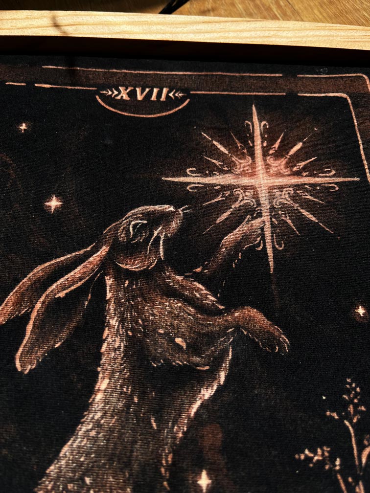 Hand-painted bleach art wall hanging of The Star tarot card, featuring a hare reaching toward a star, wood dowel frame with black fringe