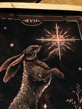 Hand-painted bleach art wall hanging of The Star tarot card, featuring a hare reaching toward a star, wood dowel frame with black fringe
