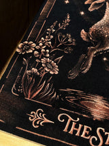 Hand-painted bleach art wall hanging of The Star tarot card, featuring a hare reaching toward a star, wood dowel frame with black fringe