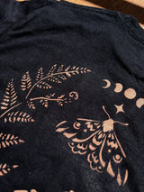 Close-up detail of stencil bleach art mushroom design on black fabric, moth and moon detail close up