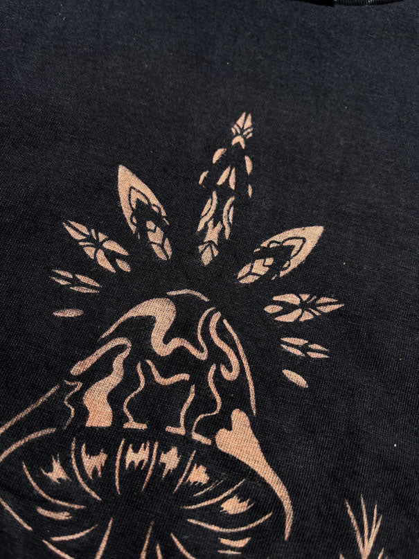 close up of stencil bleach art t-shirt with a single mushroom design surrounded by leaves and a star, on black fabric
