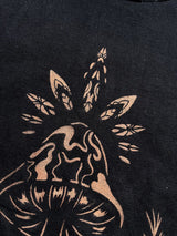 close up of stencil bleach art t-shirt with a single mushroom design surrounded by leaves and a star, on black fabric