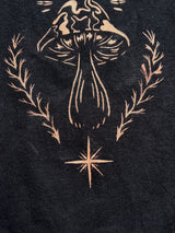 close up of stencil bleach art t-shirt with a single mushroom design surrounded by leaves and a star, on black fabric
