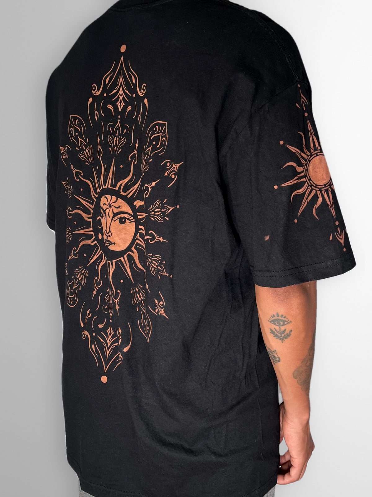 Black T-shirt with a large bleach-painted sun and moon mandala on the back and a sun on the sleeve, side view