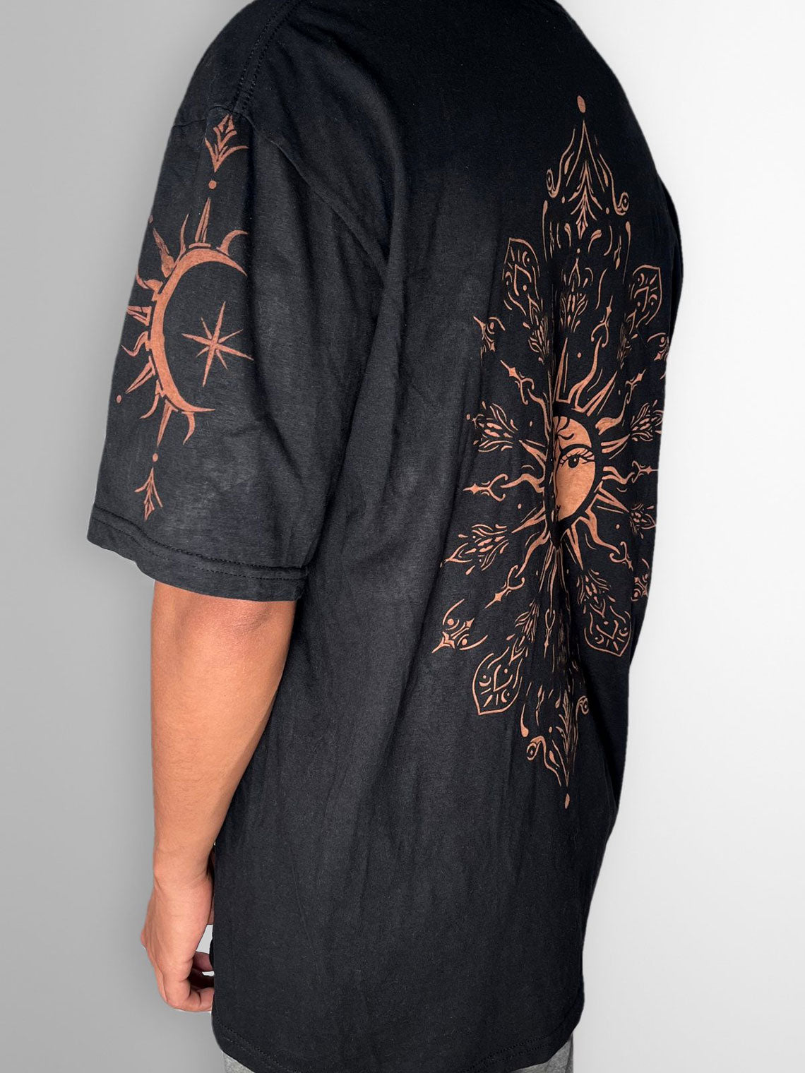 Black T-shirt with a bleach-painted sun and moon mandala on the back and a crescent moon with star on the sleeve, side view