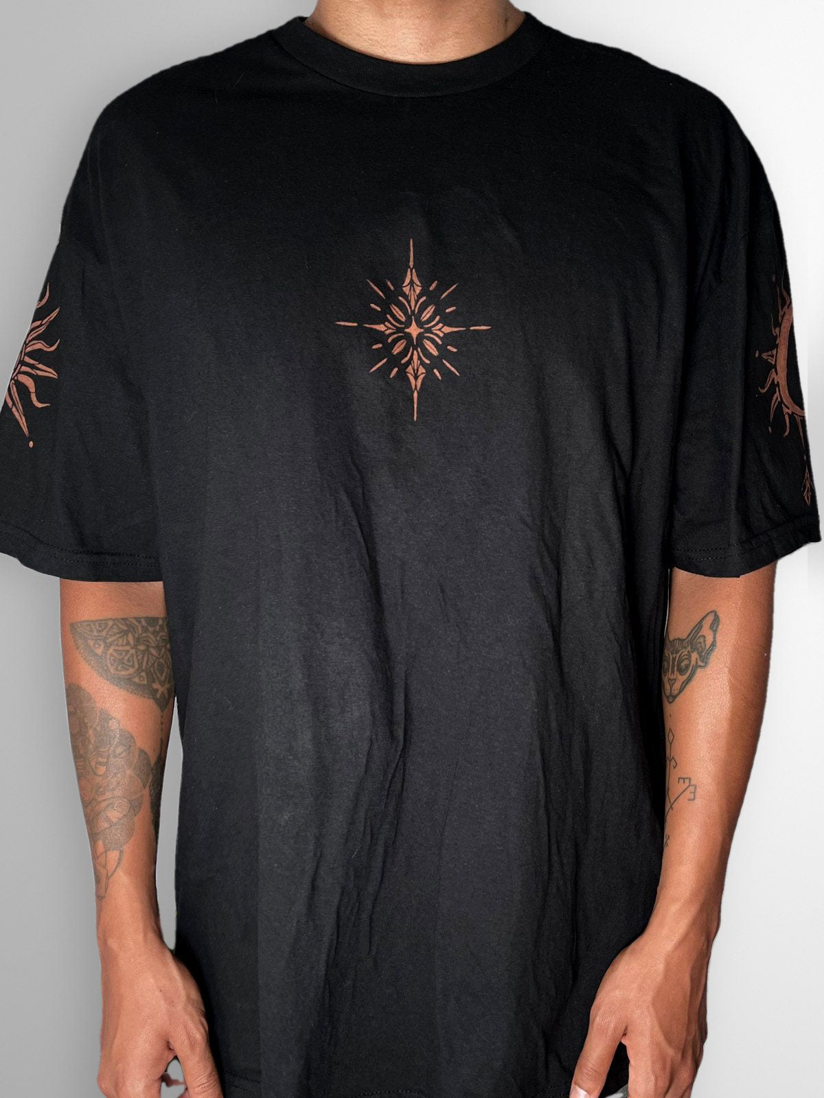 Front of a black T-shirt with a small bleach-painted starburst on the chest and sun and moon designs on the sleeves