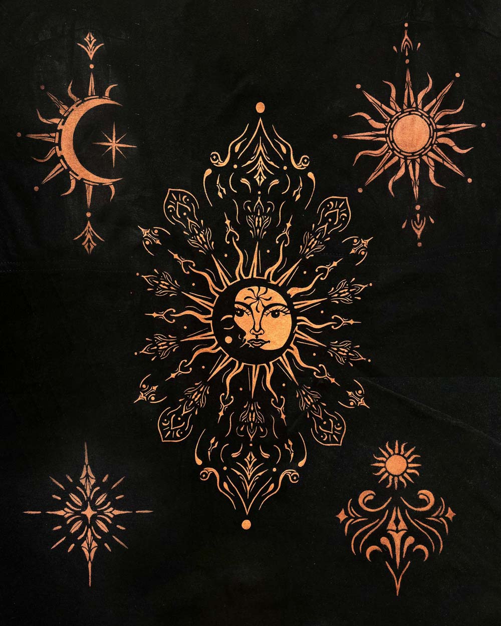 Bleach art on fabric featuring a central sun and moon design in a warm orange-gold tone, surrounded by four additional celestial and ornamental motifs. Full stencil bleach shirt pack